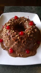 Chocolate bundt cake with frosting and topped with cherries and pecans