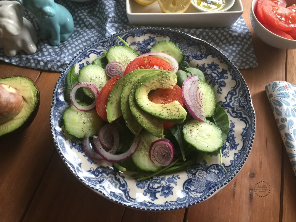 A fresh salad made with spinach, avocado, tomato, cucumber and purple onions